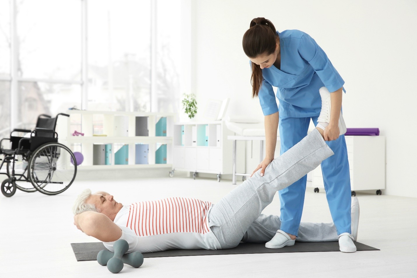 A healthcare professional assisting a patient with leg exercises in a bright, modern therapy room