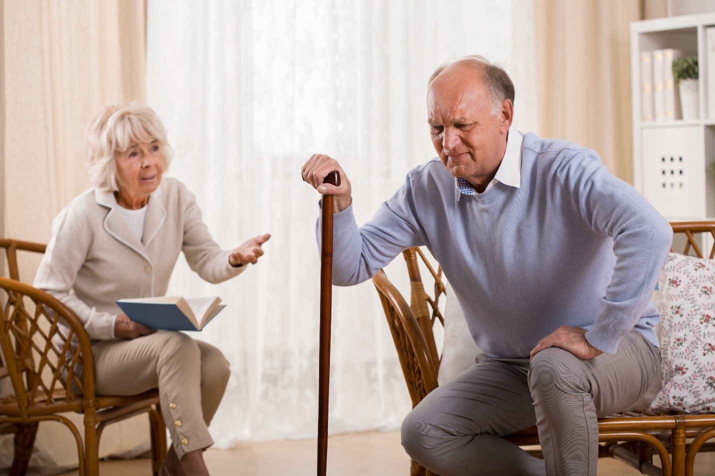 An elderly man holding his lower back in pain while his wife looks on concerned