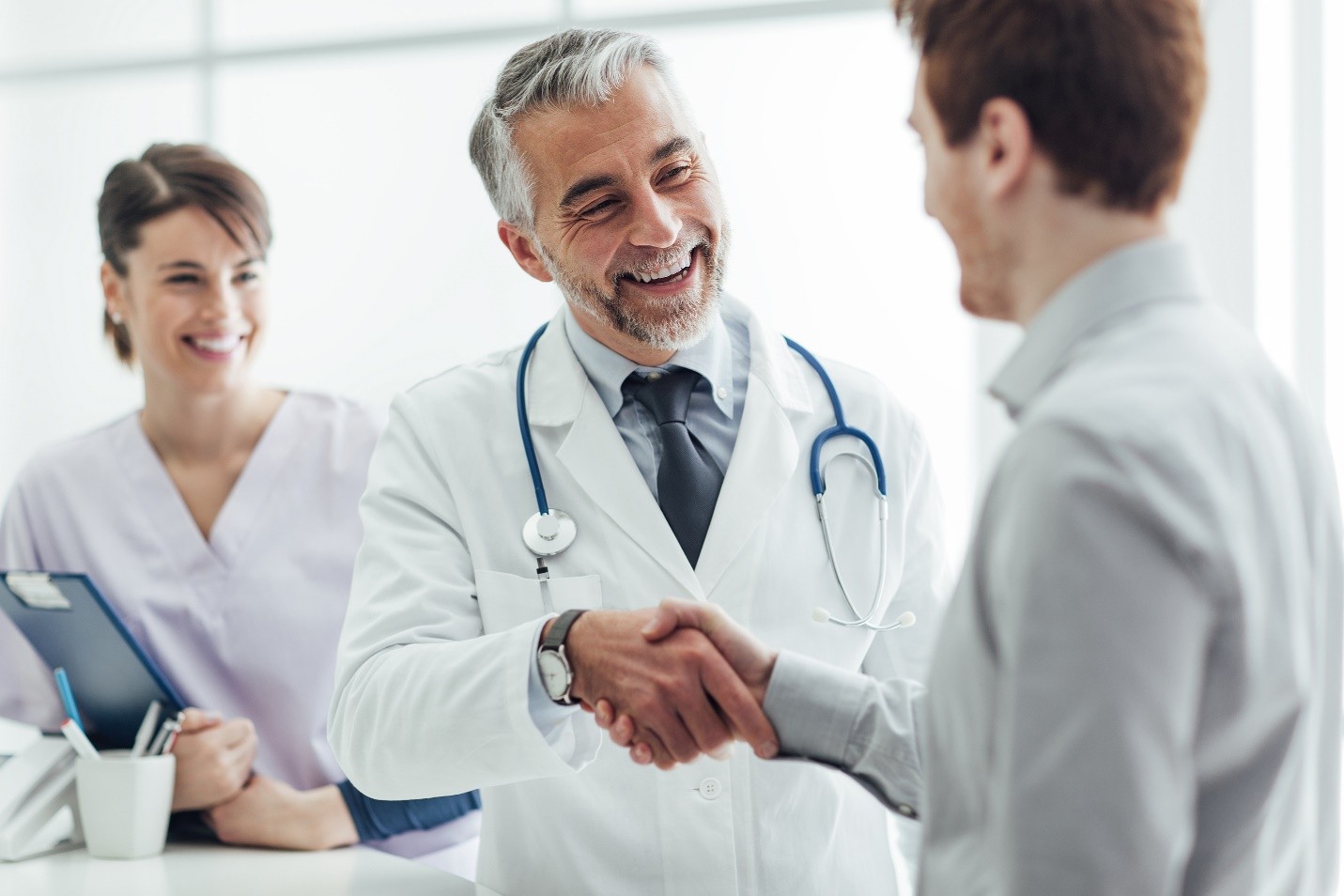 A doctor shaking hands with a patient while a nurse looks on