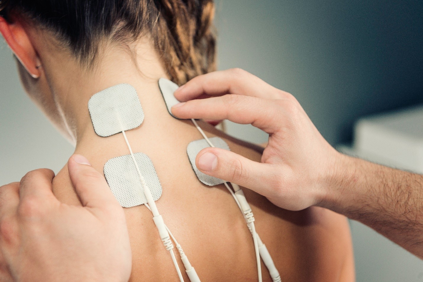 Person receiving physical therapy with electrodes attached to their neck and shoulder area