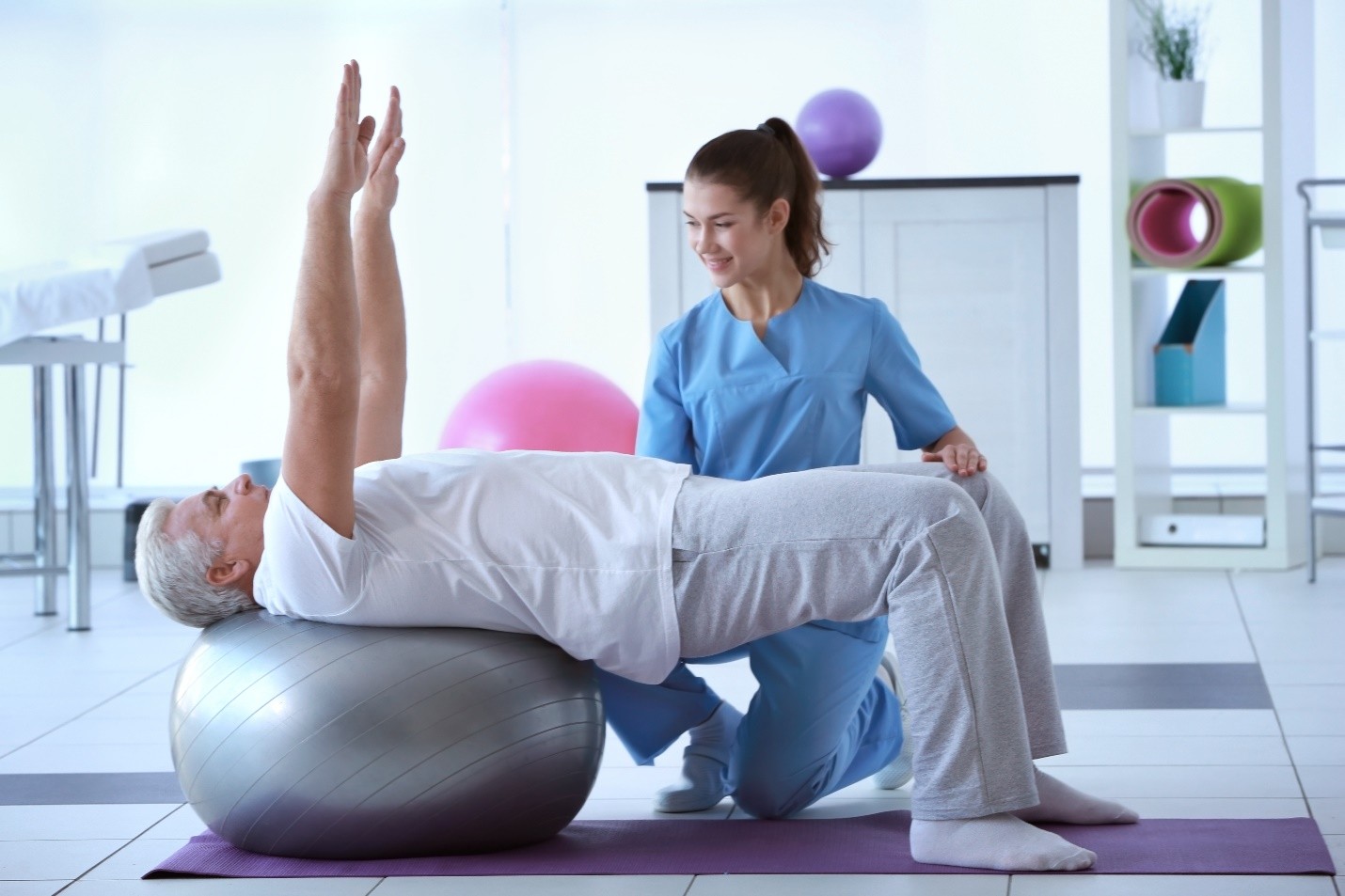 Physiotherapist assisting an elderly man with exercises on a large exercise ball