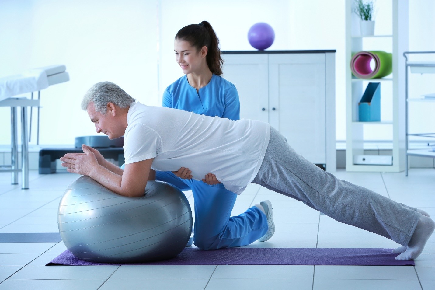 Physiotherapist assisting a patient with a plank exercise on an exercise ball