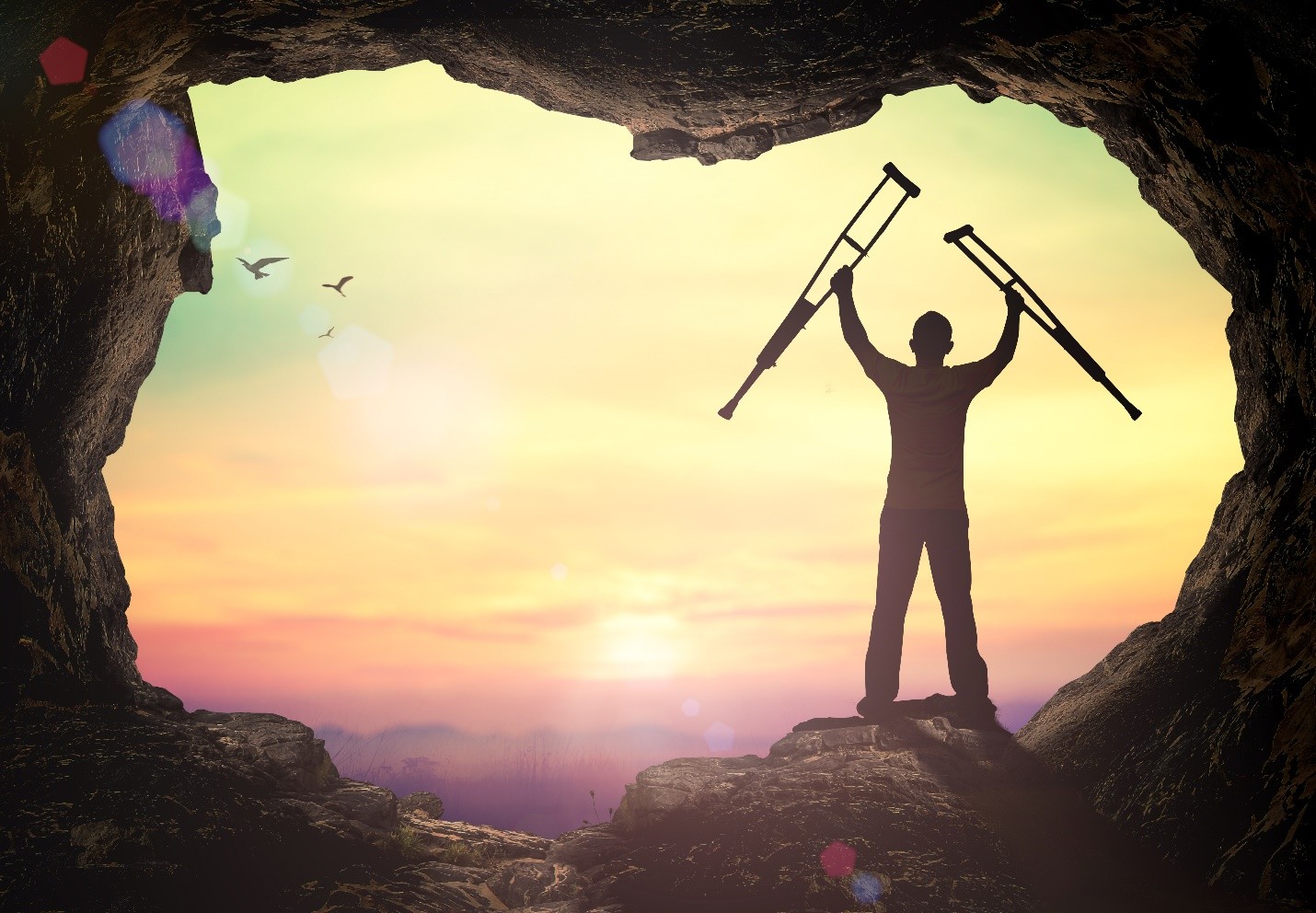 A silhouette of a person standing in a cave opening, holding crutches up triumphantly against a sunrise background